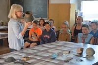 archeolog pokazuje dzieciom w sali dydaktycznej eksponat archeologiczny
